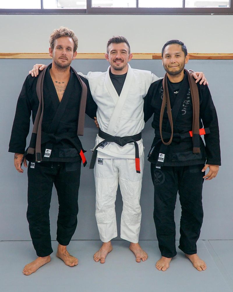 Black belts Tanner, Nick Bohli and Mark Lazatin standing arm in arm on the mat, two with brown belts over their shoulders