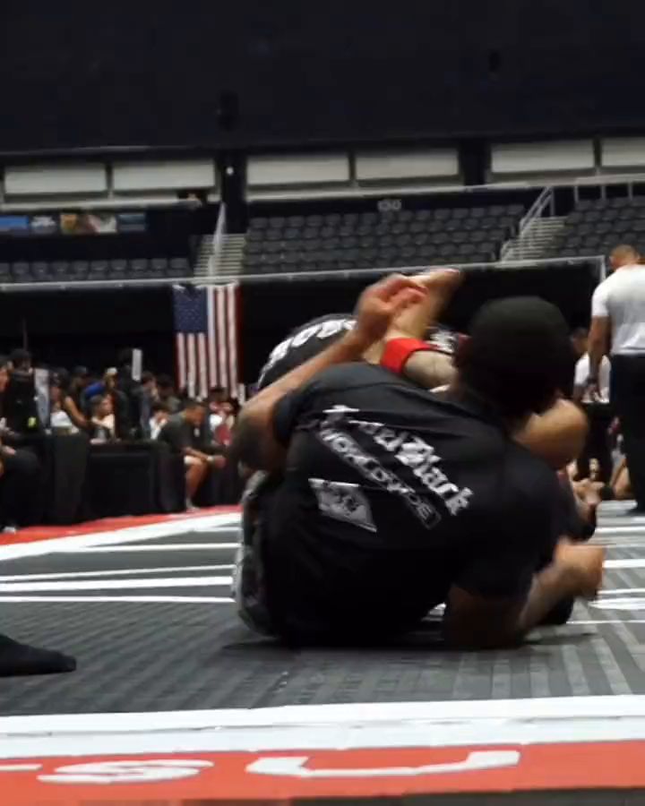 Two grapplers in black rash guards wrestling for position at a no-gi tournament