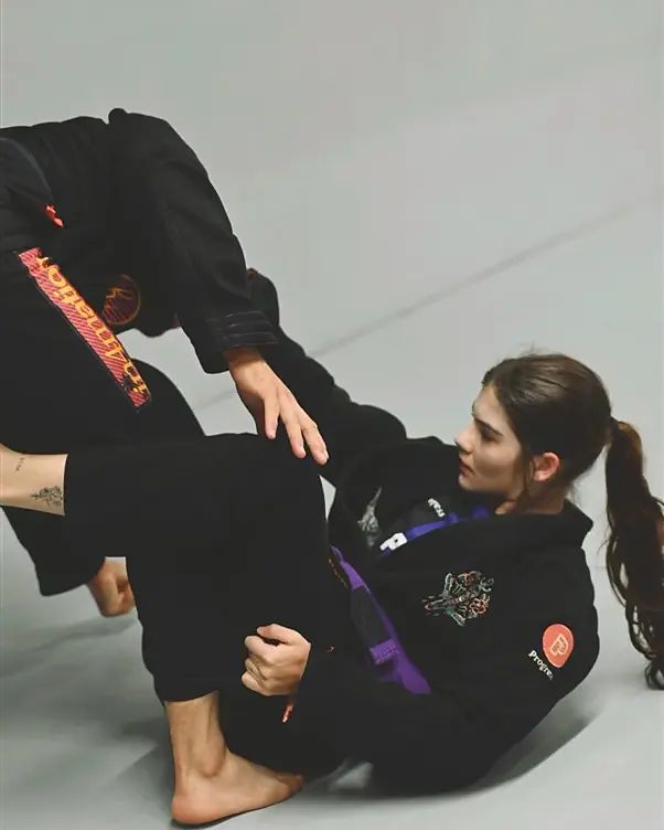 A purple belt in a black gi playing open guard